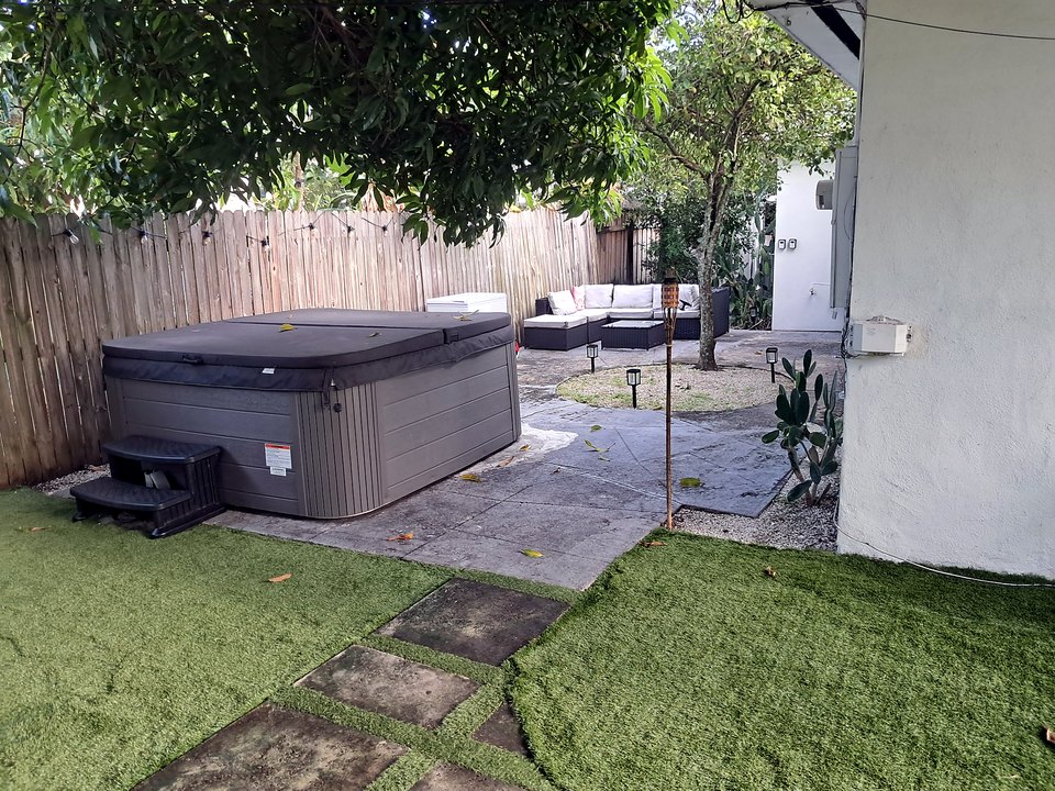 Hot tub on the patio with an outdoor sectional lounge beneath mature trees