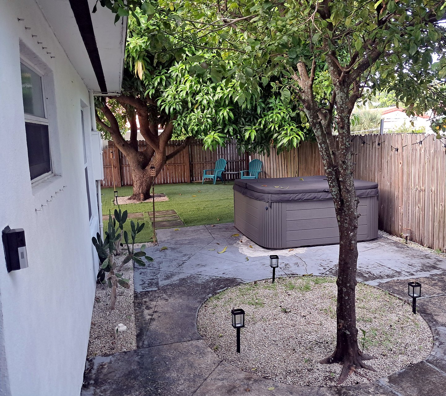 Looking past the hot tub on the stone patio toward the lawn, fruit trees and the privacy fence